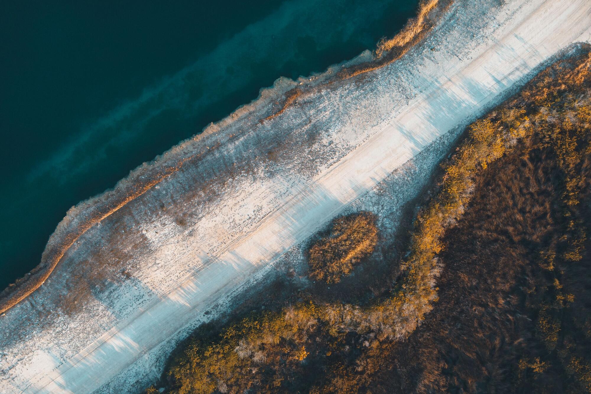 Straight-down aerial view of a Gulf coast shoreline, dark open water meeting a curving white sandbar and coastal scrub